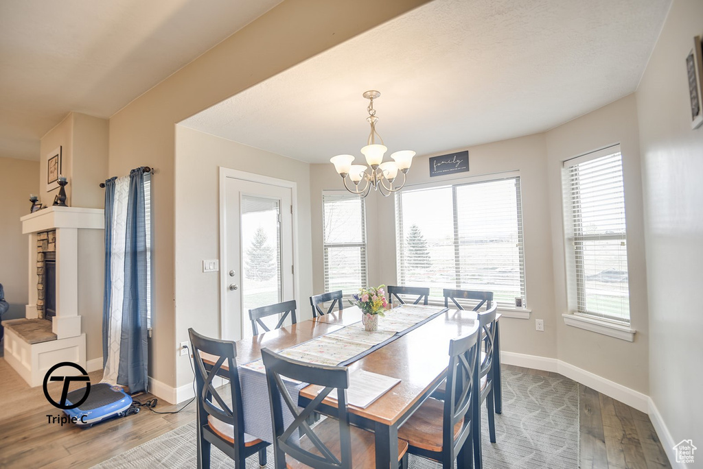 Dining area with an inviting chandelier, a fireplace with raised hearth, wood finished floors, and baseboards