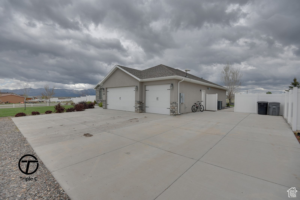 View of side of property with stucco siding, an attached garage, fence, concrete driveway, and a shingled roof