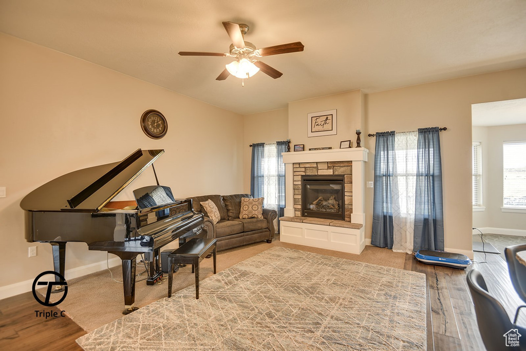 Living room with a stone fireplace, wood finished floors, baseboards, and ceiling fan