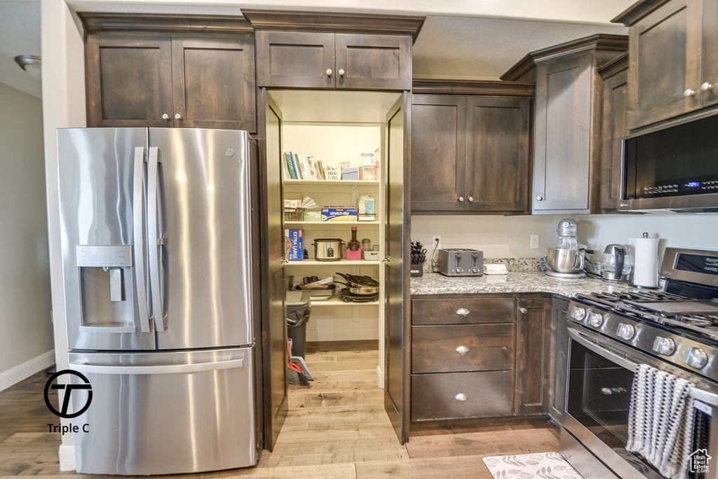 Kitchen with appliances with stainless steel finishes, dark brown cabinets, and light wood-style flooring