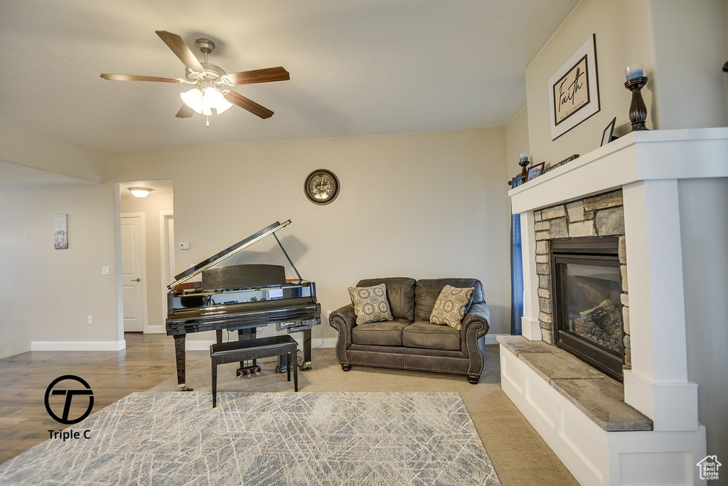 Living area with a ceiling fan, a stone fireplace, and baseboards