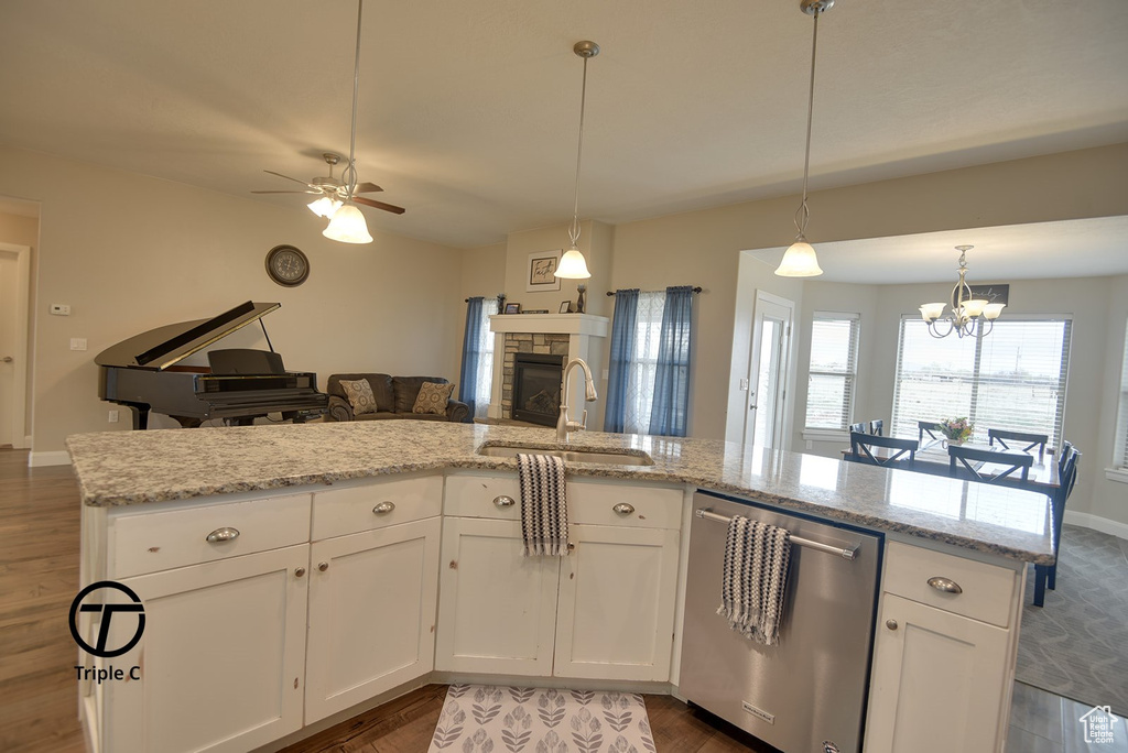 Kitchen featuring dishwasher, a stone fireplace, a sink, open floor plan, and dark wood-type flooring