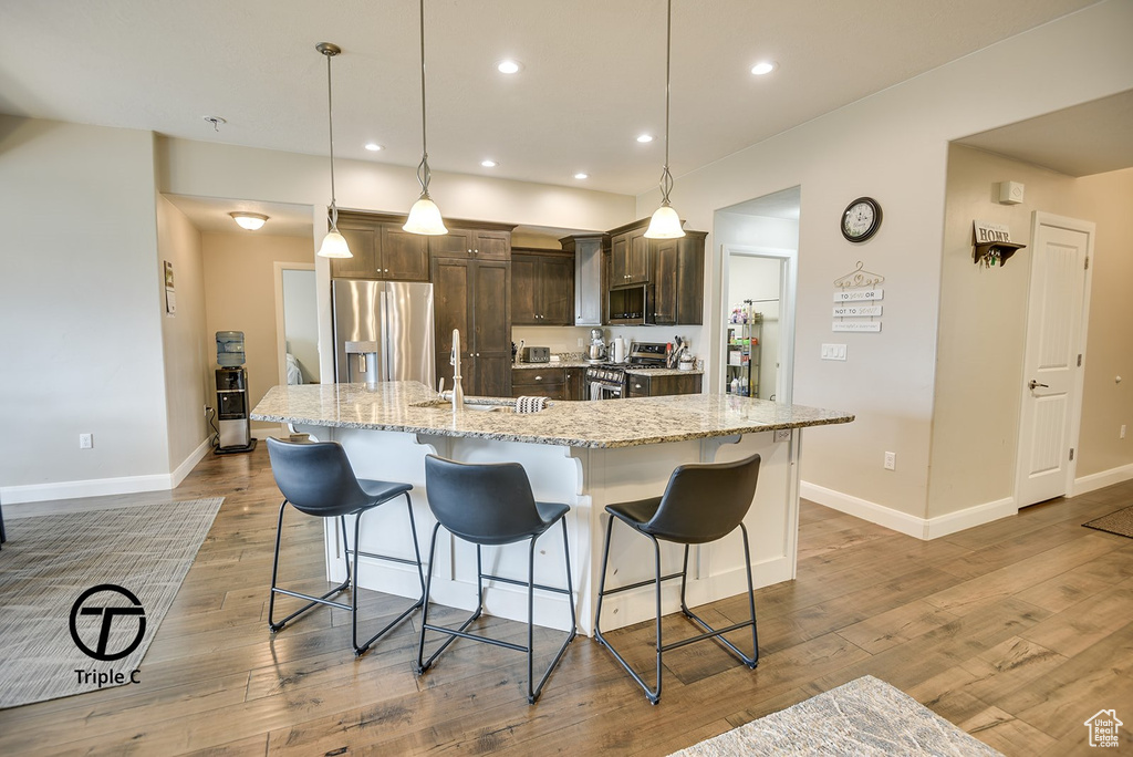 Kitchen with dark brown cabinets, a kitchen bar, a sink, appliances with stainless steel finishes, and a spacious island
