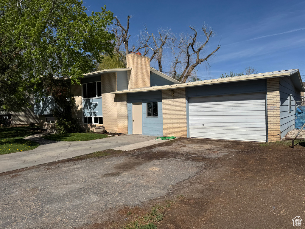 View of front facade featuring a chimney, brick siding, an attached garage, and aphalt driveway