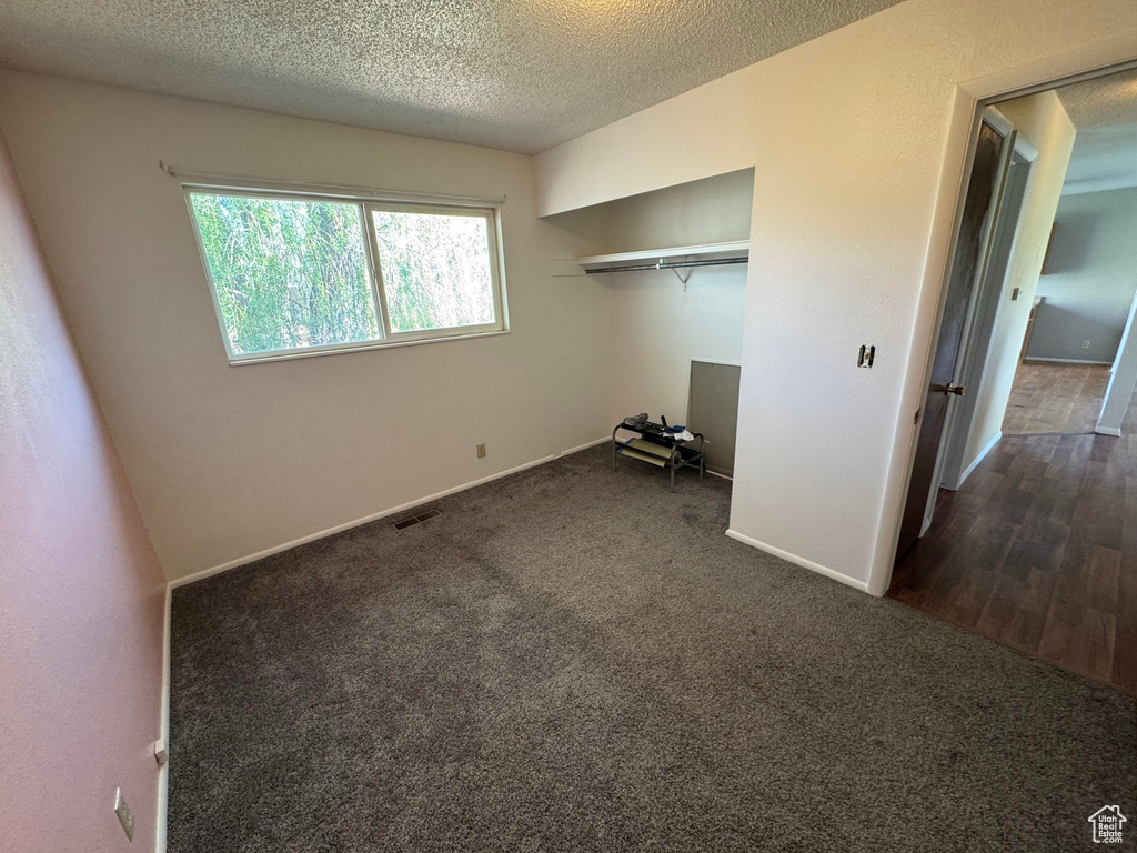 Unfurnished bedroom featuring dark colored carpet, baseboards, a textured ceiling, and a closet