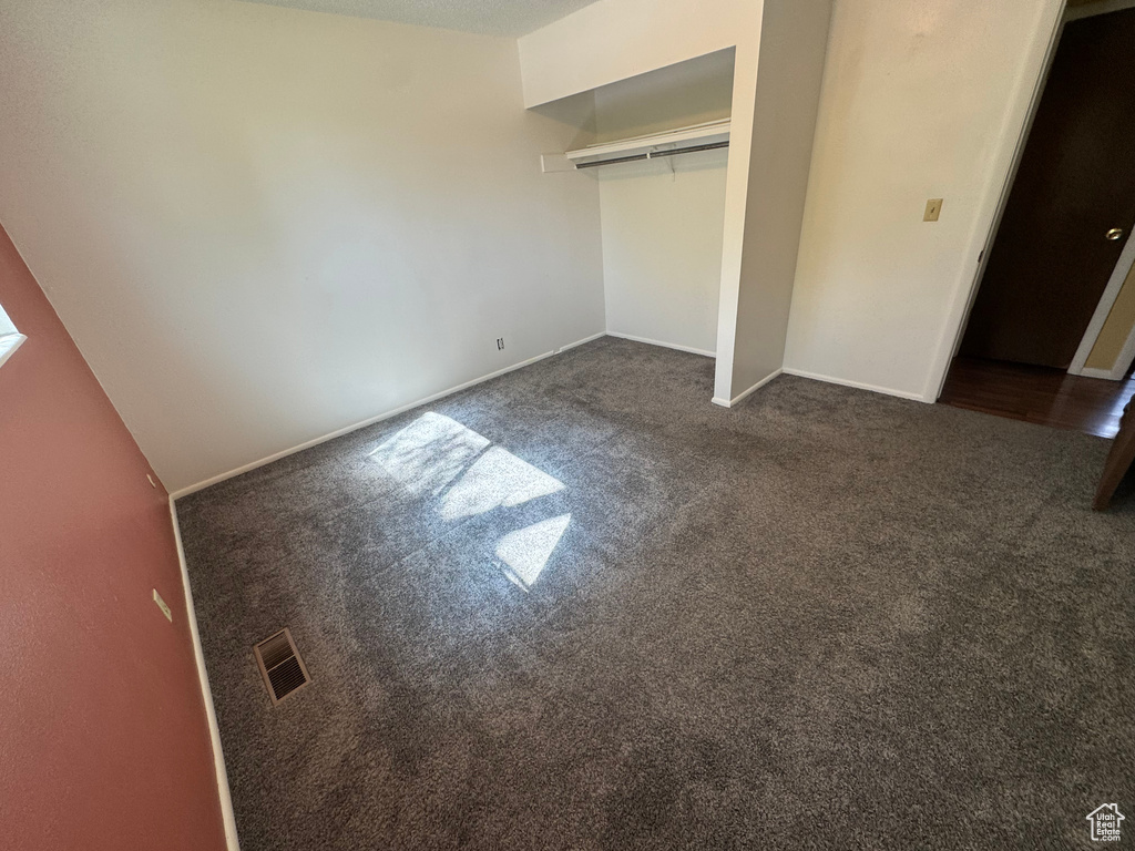 Unfurnished bedroom with dark carpet, a closet, and baseboards