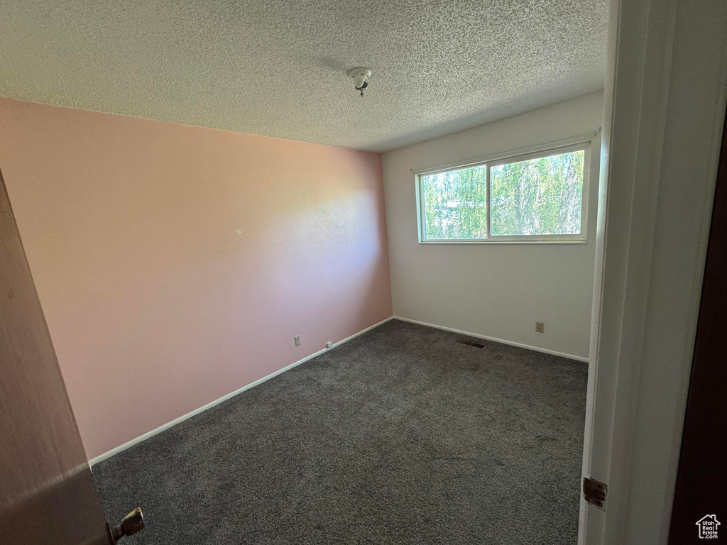 Spare room featuring a textured ceiling, dark colored carpet, and baseboards