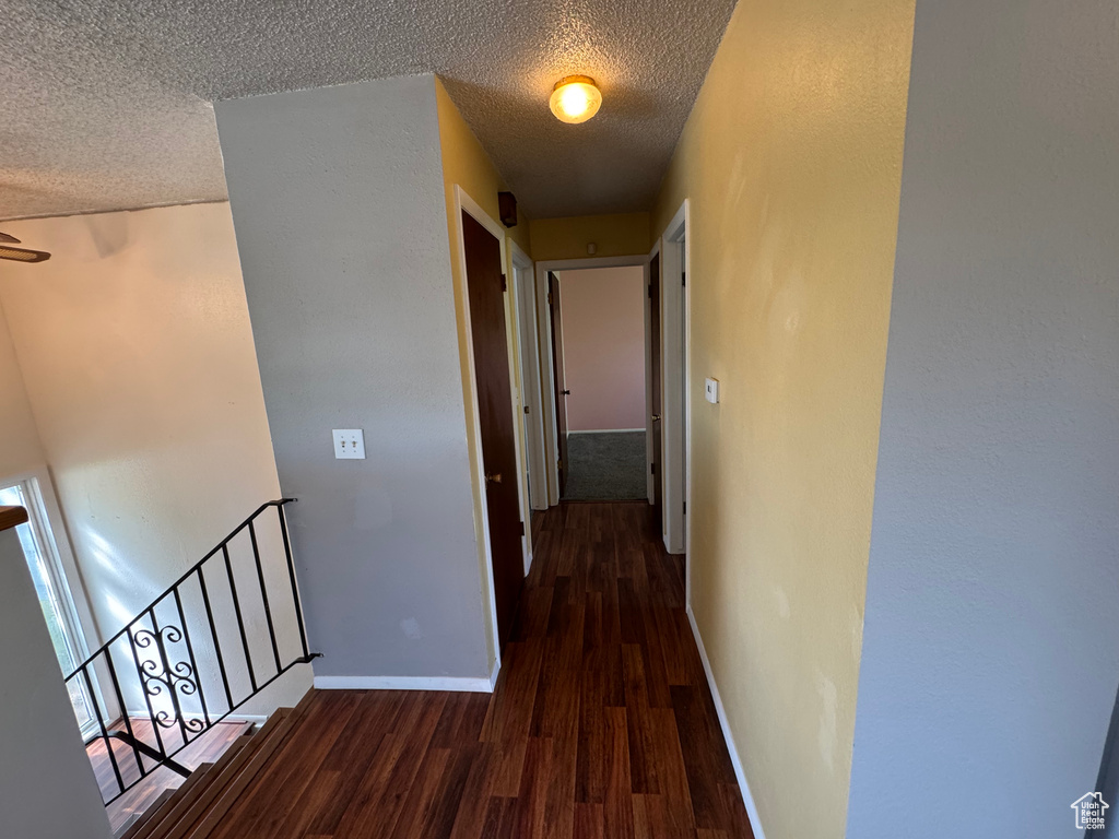 Hallway featuring dark wood finished floors, an upstairs landing, baseboards, and a textured ceiling