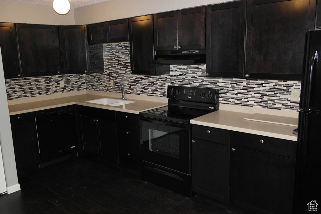 Kitchen with under cabinet range hood, decorative backsplash, black appliances, and a sink