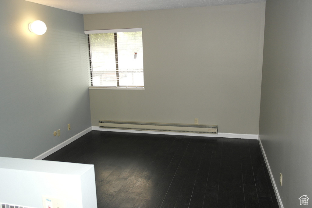 Spare room featuring baseboards, a baseboard radiator, and dark wood-type flooring