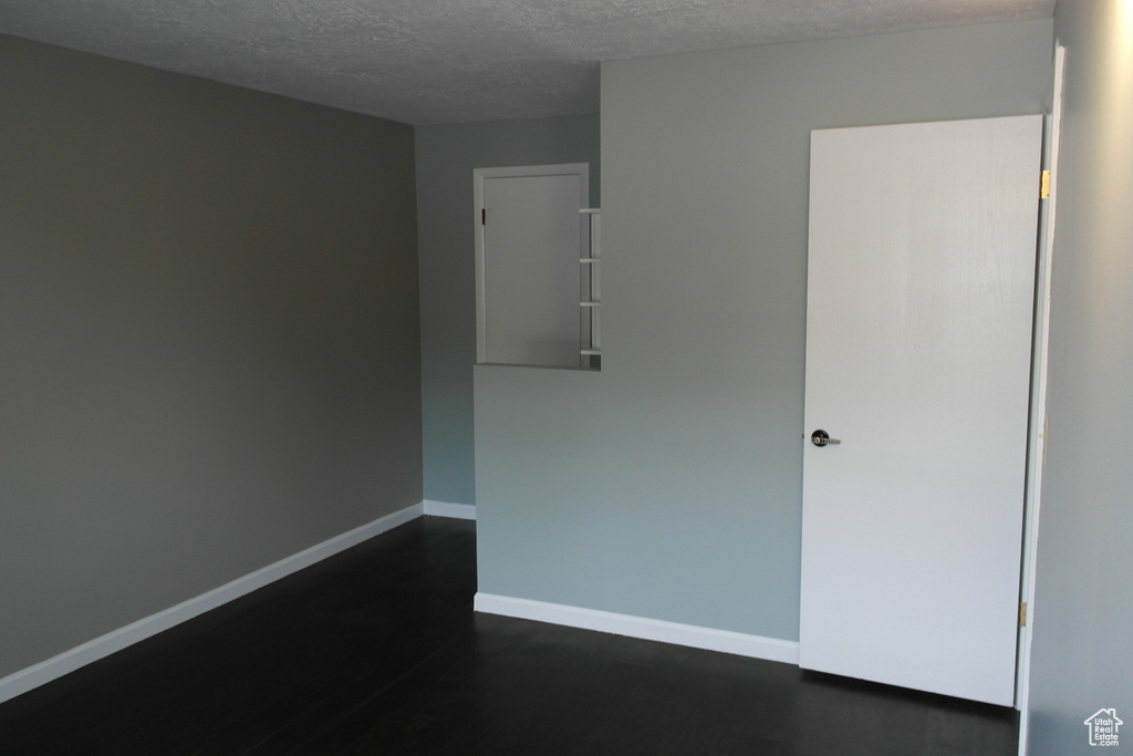 Empty room featuring baseboards, dark wood finished floors, and a textured ceiling