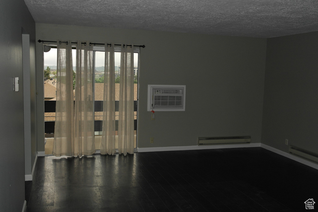 Empty room with a textured ceiling, baseboards, baseboard heating, and wood finished floors