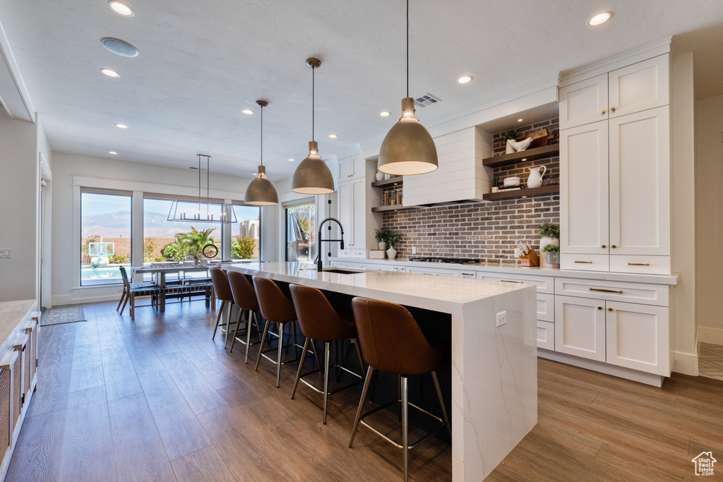 Kitchen with open shelves, a kitchen breakfast bar, light wood-style flooring, white cabinetry, and a center island with sink