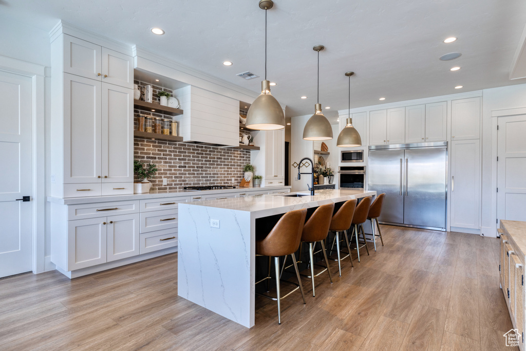 Kitchen featuring open shelves, a sink, built in appliances, white cabinetry, and tasteful backsplash
