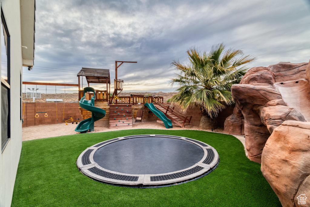 View of playground featuring fence, a trampoline, and a lawn