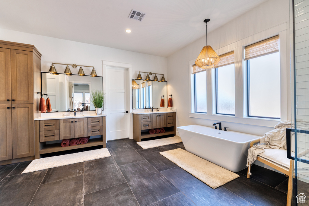 Full bathroom featuring a soaking tub, visible vents, two vanities, and a wealth of natural light