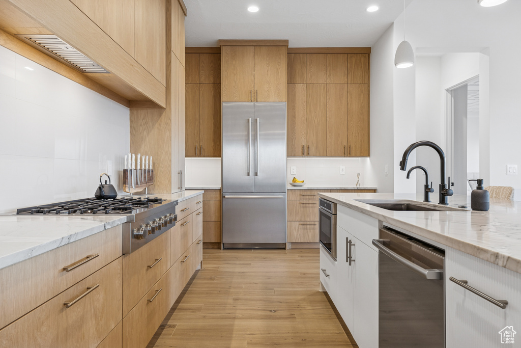 Kitchen with light wood finished floors, a sink, stainless steel appliances, light stone counters, and recessed lighting