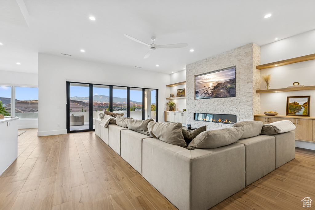 Living room featuring a ceiling fan, a stone fireplace, light wood-style flooring, and recessed lighting