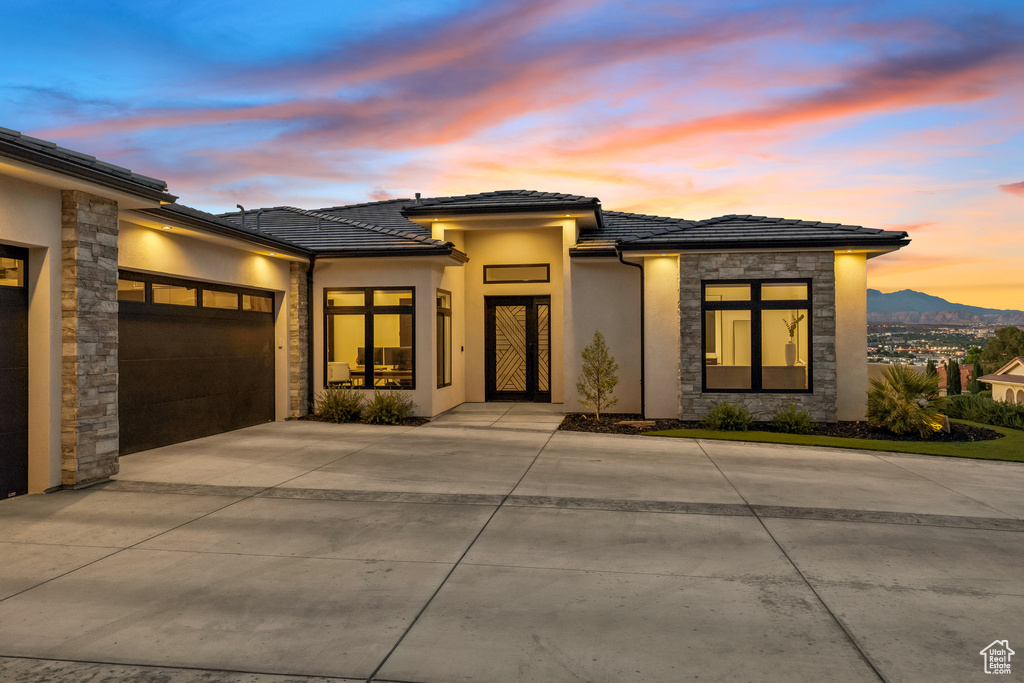 Prairie-style home with stone siding, an attached garage, a tiled roof, stucco siding, and driveway