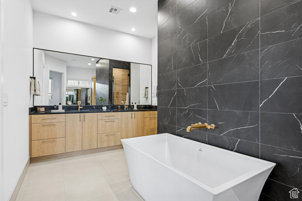 Full bathroom featuring tile walls, visible vents, recessed lighting, a soaking tub, and double vanity