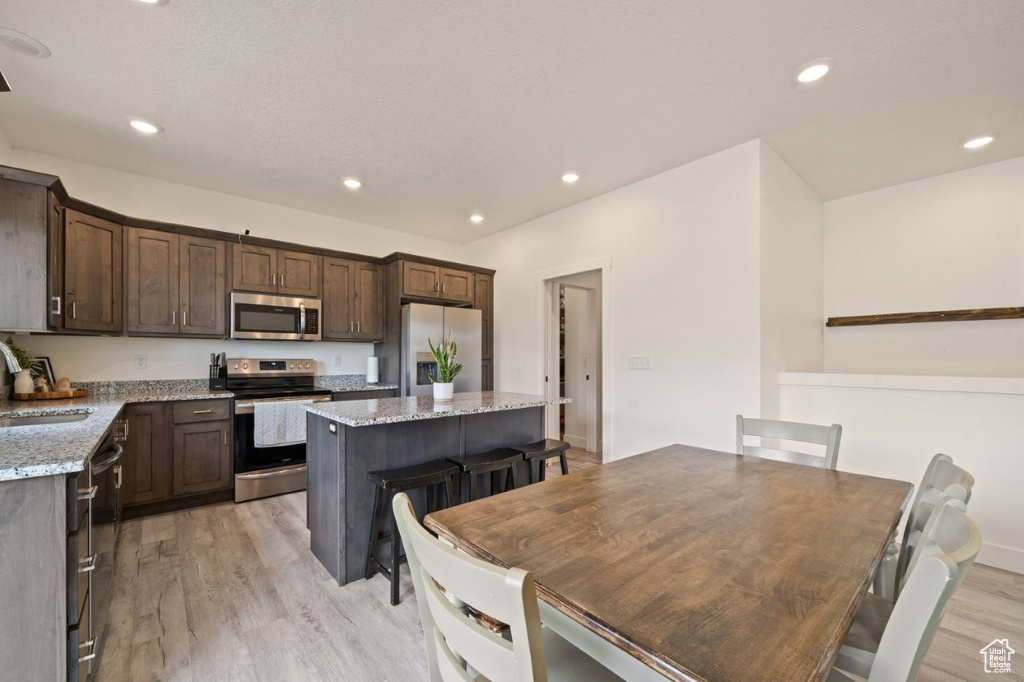 Kitchen featuring light wood finished floors, a center island, a sink, stainless steel appliances, and dark brown cabinetry
