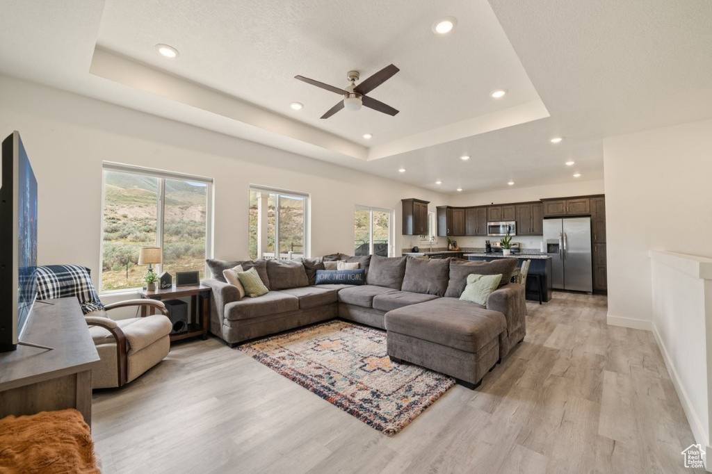 Living area with light wood-type flooring, recessed lighting, a ceiling fan, a raised ceiling, and baseboards