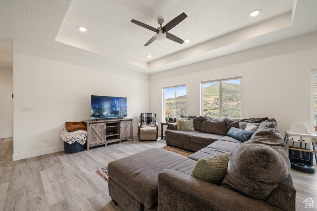 Living room featuring a ceiling fan, light wood-style flooring, recessed lighting, baseboards, and a raised ceiling