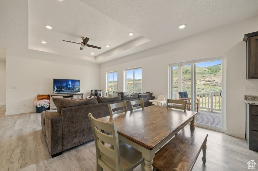 Dining space with a ceiling fan, baseboards, light wood finished floors, and a tray ceiling