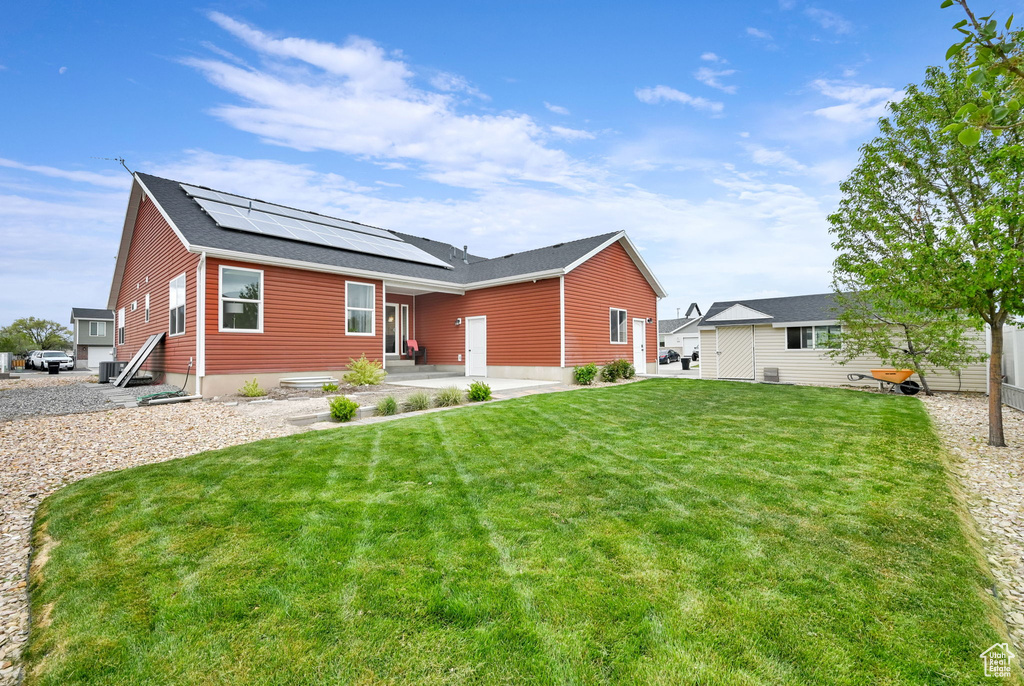 View of front of home with roof with shingles, a patio, entry steps, solar panels, and a front lawn