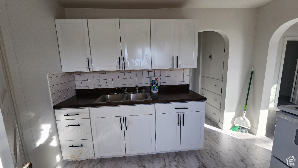 Kitchen featuring white cabinets, dark countertops, decorative backsplash, and a sink