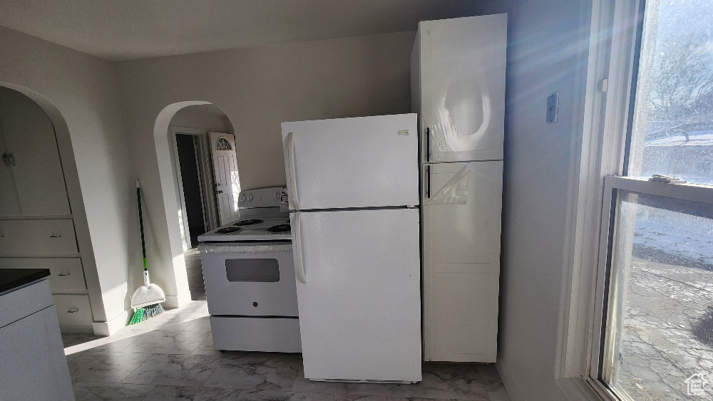 Kitchen with white appliances, arched walkways, dark countertops, and marble finish floor