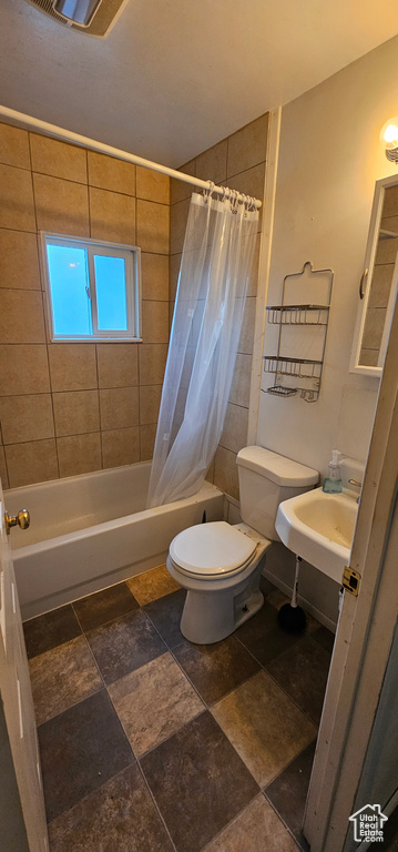 Bathroom with toilet, stone finish flooring, a sink, shower / tub combo with curtain, and visible vents