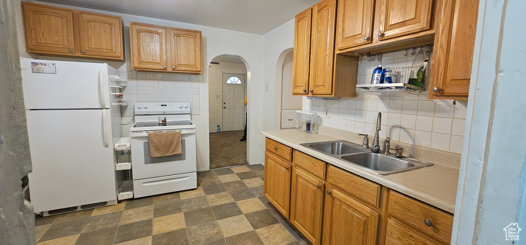Kitchen featuring white appliances, a sink, arched walkways, light countertops, and tasteful backsplash