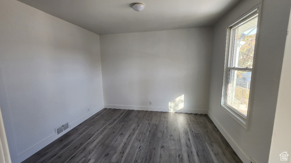 Empty room featuring dark wood finished floors, visible vents, and baseboards