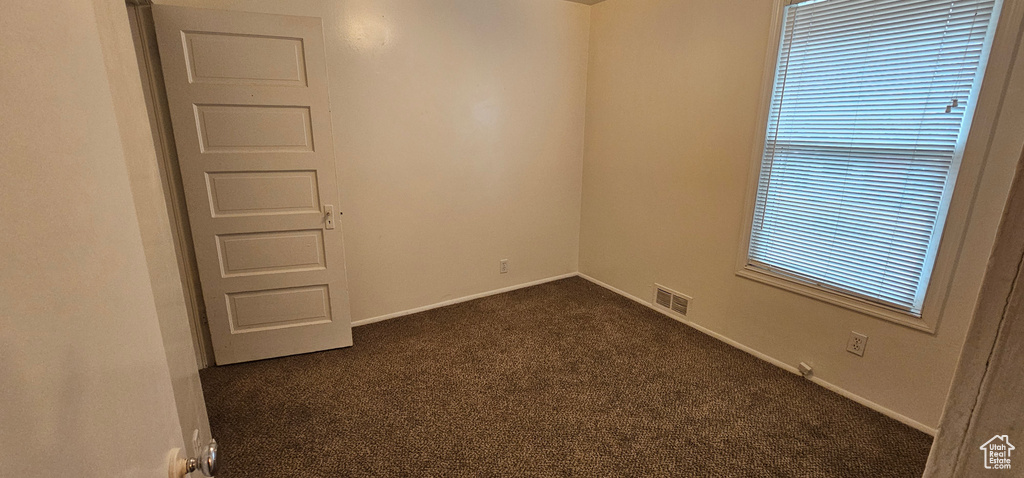 Spare room with baseboards, visible vents, and dark carpet