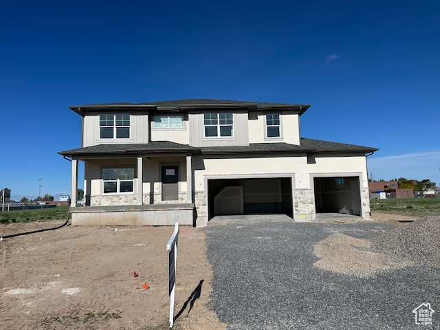 View of front facade featuring stucco siding, a garage, gravel driveway, and stone siding