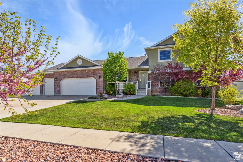 View of front of property with a porch, brick siding, driveway, a garage, and a front yard