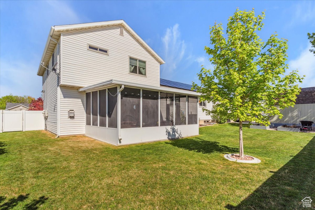 Back of house featuring a sunroom, fence, and a lawn