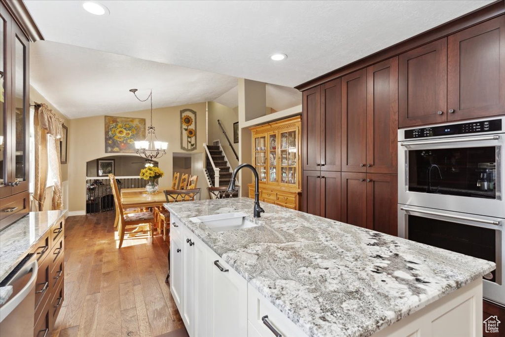 Kitchen with a sink, stainless steel double oven, vaulted ceiling, light wood-style flooring, and a notable chandelier