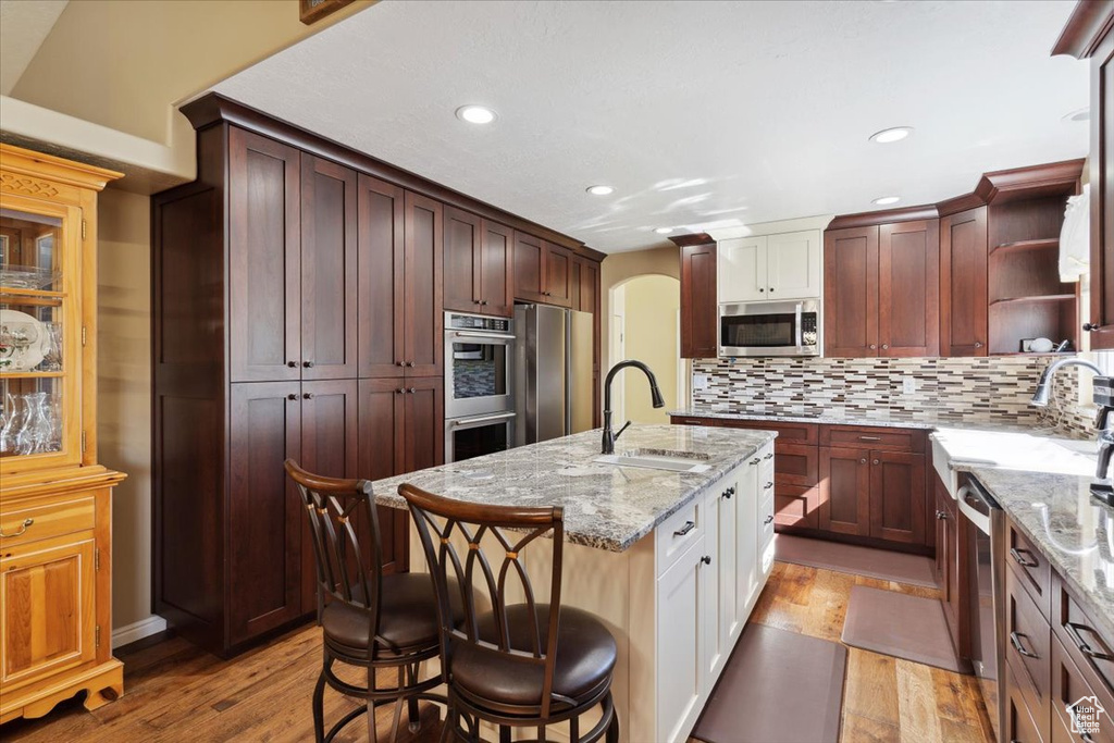 Kitchen with arched walkways, light wood finished floors, appliances with stainless steel finishes, and a sink