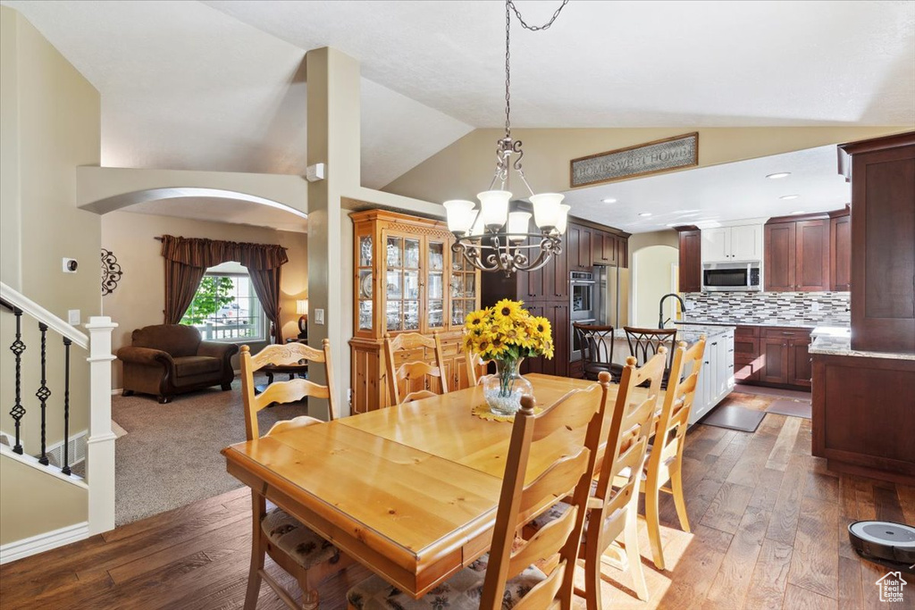 Dining space with a chandelier, high vaulted ceiling, hardwood / wood-style flooring, arched walkways, and stairway
