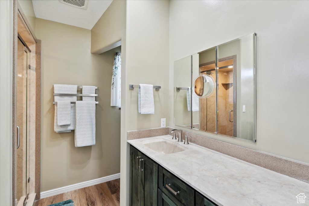 Full bathroom with wood finished floors, visible vents, baseboards, a shower stall, and vanity