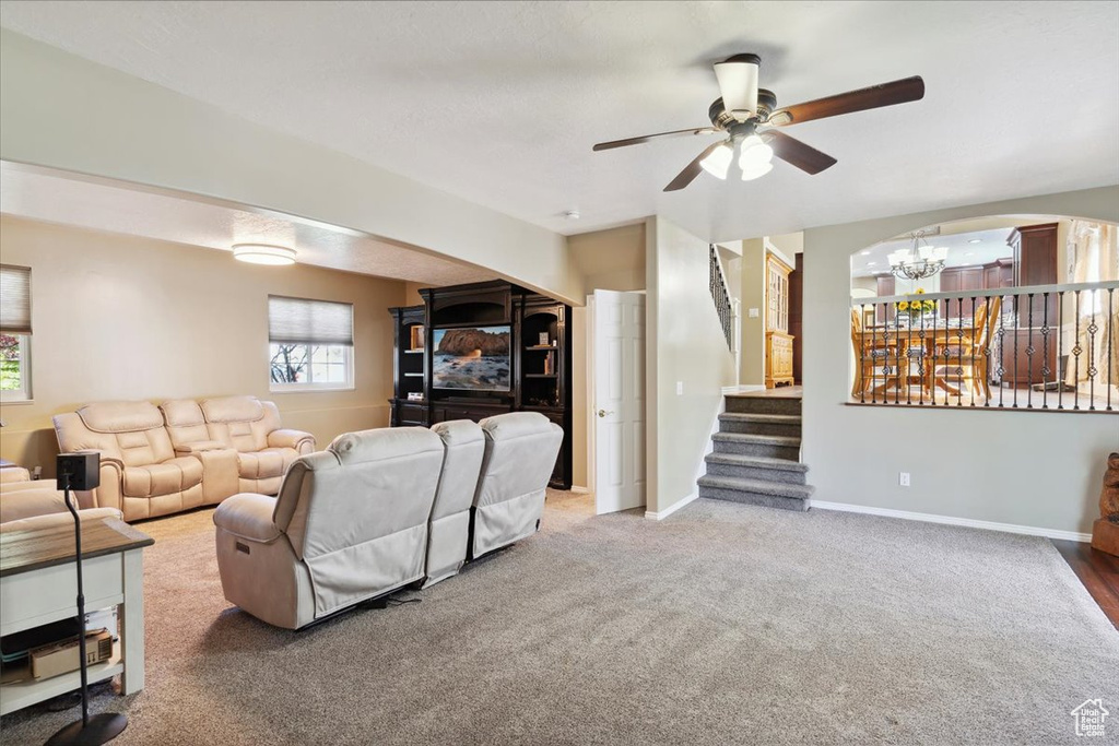 Living area with carpet flooring, stairway, baseboards, and ceiling fan with notable chandelier