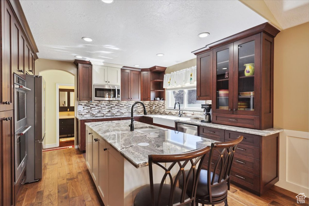 Kitchen featuring light wood-type flooring, backsplash, appliances with stainless steel finishes, and a sink