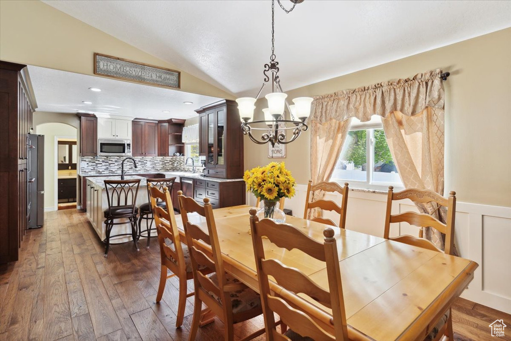 Dining area with lofted ceiling, dark wood-type flooring, a chandelier, arched walkways, and wainscoting