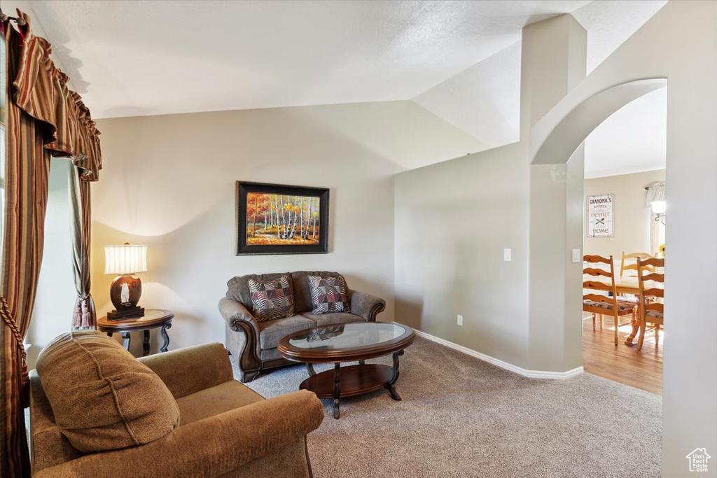 Living area with carpet floors, lofted ceiling, arched walkways, and baseboards