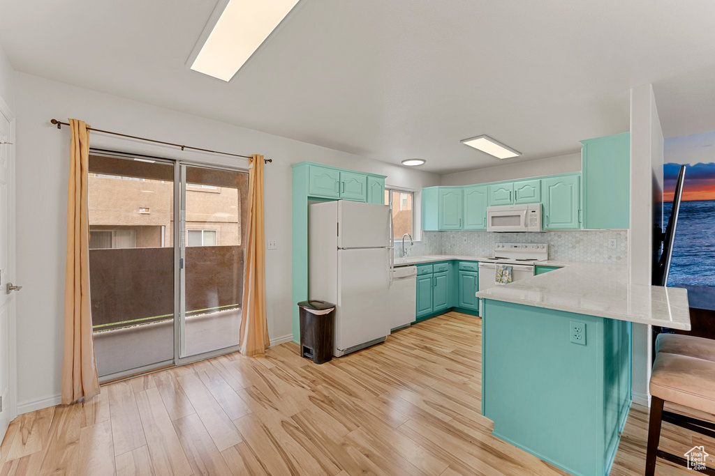 Kitchen with a breakfast bar area, light countertops, a peninsula, light wood-style floors, and white appliances