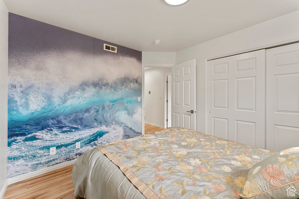 Bedroom with baseboards, visible vents, wood finished floors, and a closet