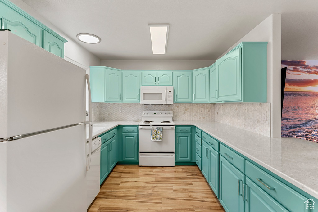 Kitchen featuring light wood-type flooring, light countertops, decorative backsplash, and white appliances