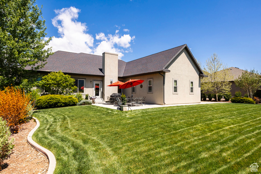 Back of property featuring a lawn, a chimney, stucco siding, and a patio
